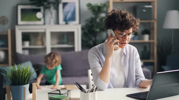 Angry Freelancer Talking on Phone Using Laptop While Her Son Playing in Room