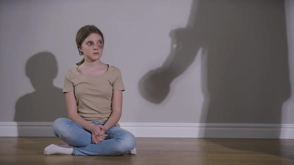 Wide Shot Scared Teenage Caucasian Girl with Bruised Face Sitting on Floor at Wall with Parent