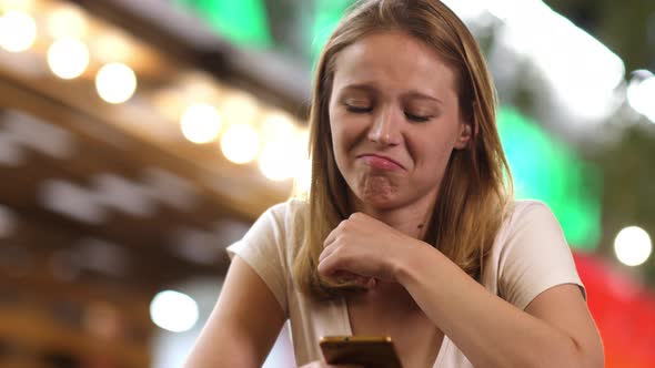 Disappointed Girl Using Her Phone in Cafe in the Evening
