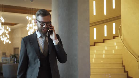 Young Man in Suit Walking Down the Hotel Lobby and Talking on Mobile Phone Business Trip