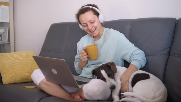 Side View of Selfemployed Woman with Bored Dog During Lockdown on Sofa with Headphones Connected to