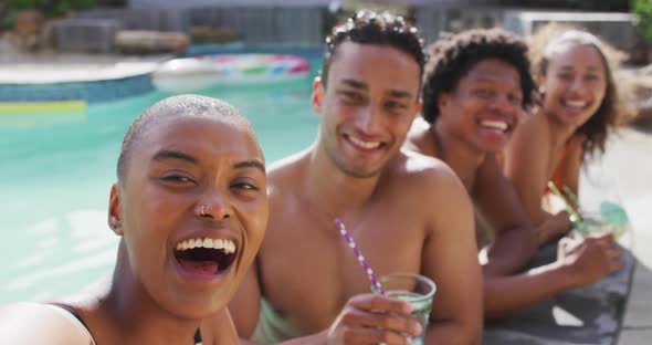 Group of diverse male and female friends making toast with drinks and laughing in pool