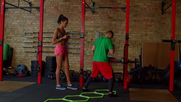 Coach Teaching Fit African Female Backward Side Straddle Hop with Agility Ladder