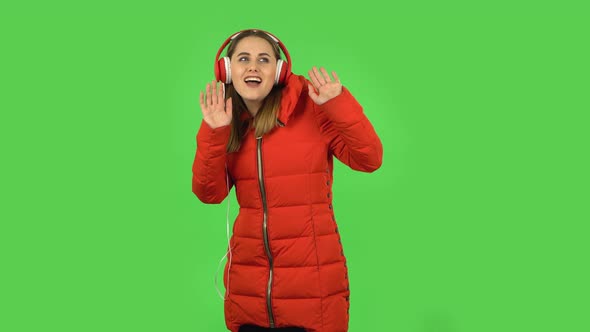 Lovely Girl in a Red Down Jacket Is Dancing and Enjoying Music in Big Red Headphones. Green Screen
