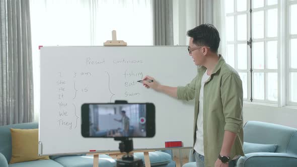 Asian Male Teacher With Glasses Shoots Video By Smartphone Camera While Teaching English At Home
