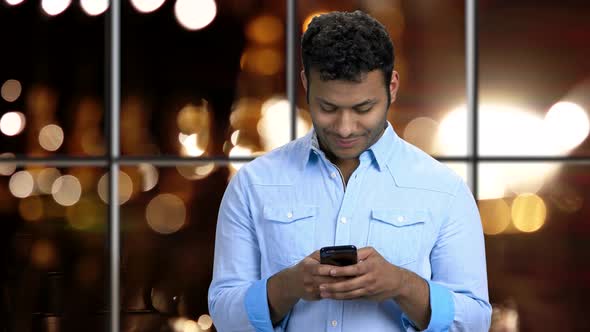 Young Smiling Man Typing Message on His Smartphone.