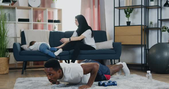 Black-Skinned Man Doing Sport Exercises on Push-Up while His Adorable Smiling Loving Muslim Wife