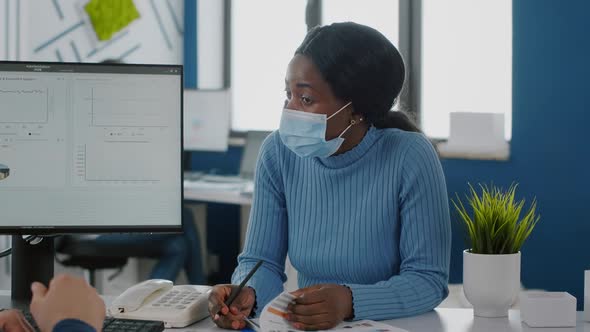 African Employee with Face Mask Explaning Project to Invalid Coworker