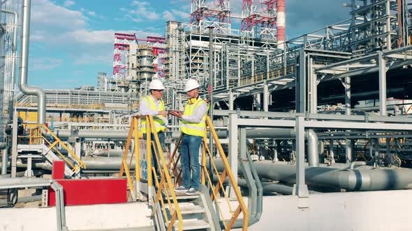 Male Partners in Hardhats are Talking at the Oilprocessing Plant