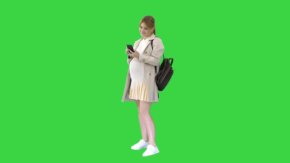 Pregnant Casual Woman Holding Cellphone Texting a Message on a Green Screen, Chroma Key.