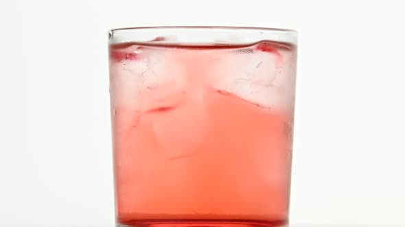 Ice cubes spin in glass of pink cocktail on white