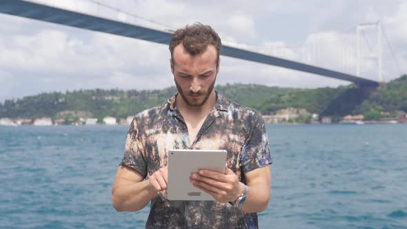 Man using tablet by the sea laughs looking at camera.