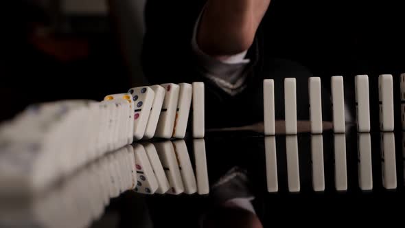 Businessman Hand Stopping Dominoes Row From Falling on a Black Background