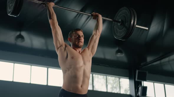 Young male athlete lifts a barbell above his head, weight training