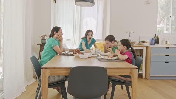 Mother and three kids eating breakfast of pancakes and fruits