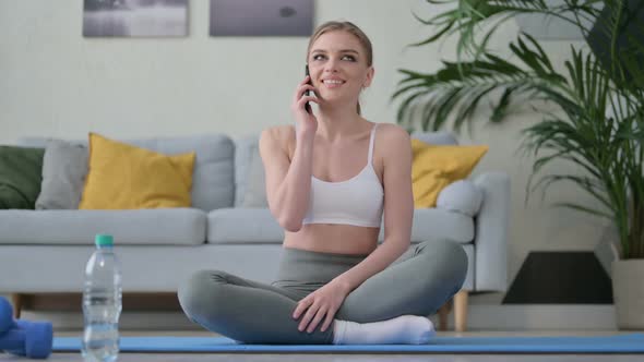 Young Woman Talking on Smartphone on Yoga Mat at Home