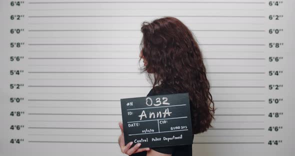 Mugshot of Woman with Curly Hair Holding Sign for Photo in Police Department While Turning to Sides