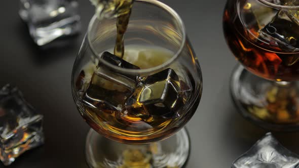 Pouring Whiskey, Cognac Into Glass with Ice Cubes. Pour of Alcohol Drink