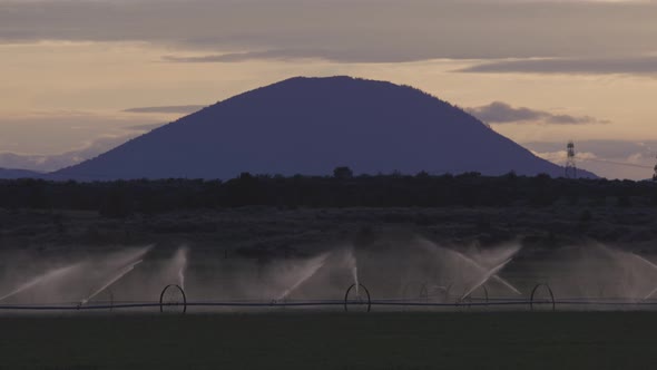 Irrigation Sprinkler System in a Farm Land Spraying Water with Mountain Landscape in Background