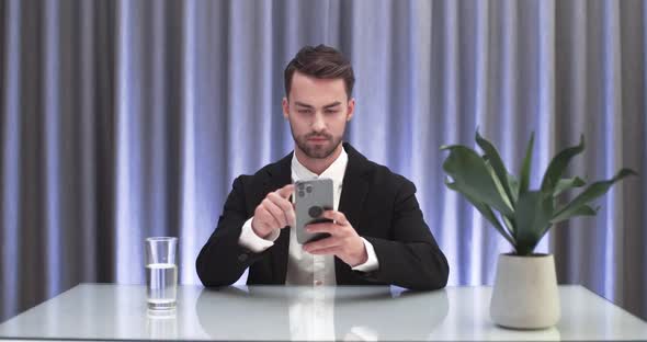 Businessman Sitting at the Table and Swipes on the Smartphone Screen Communication on the Internet