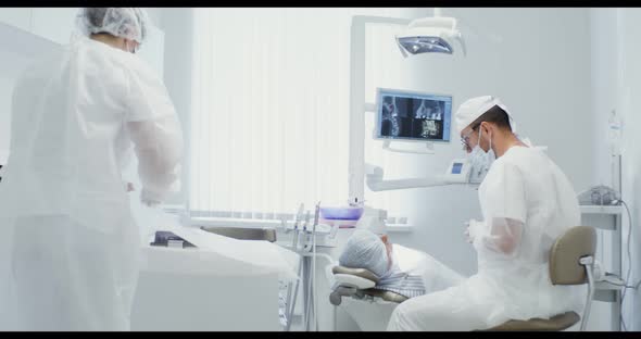 A Dentist is Talking to a Patient While a Nurse is Preparing Working Tools