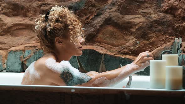 Happy beautiful young adult woman washing with shower sitting in the bathroom at home.