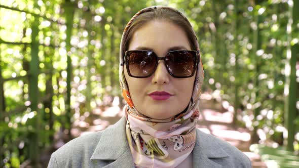 Closeup of a Woman in a Headscarf and Sunglasses Smiling in a Garden Arch