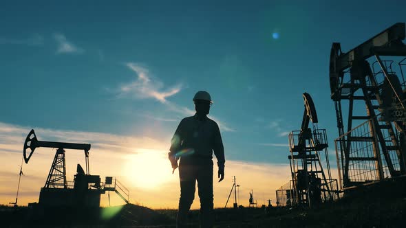 Engineer Typing on Laptop Surrounded By Oil Pumpjacks at Sunset