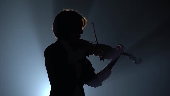 Violinist Bows the Violin on Dark Studio . Black Smoke Background. Silhouette