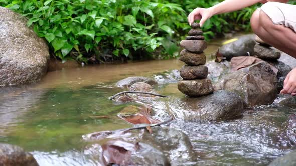 Slow motion of a woman stacking stone by the waterfall