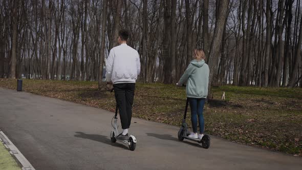 A Beautiful Couple of Young People Ride in the Park on Electric Scooters