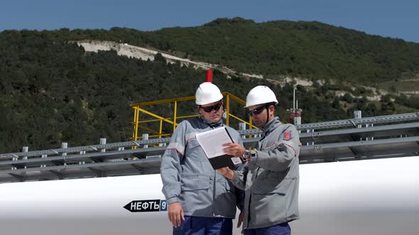 Oil workers stand at the pipe of a large oil pipeline