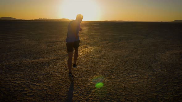 Athletic man working out with battle ropes on a dry lake at sunset