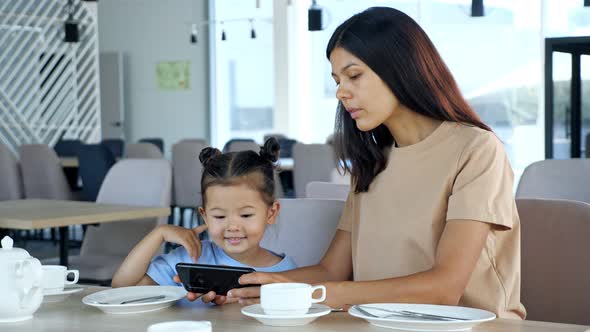 Young Woman Brunette and Small Kid Watch Video on Gadget