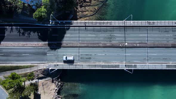 Cars and pedestrians travel across a bridge spanning across a clear water scenic creek. Drone view d