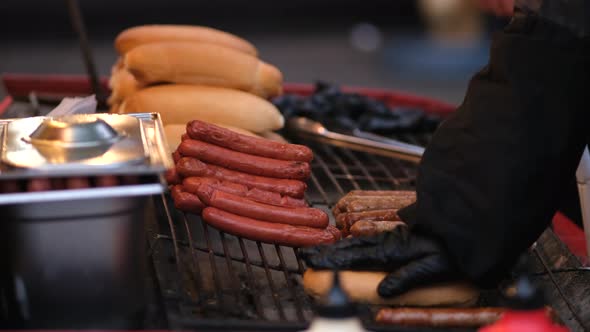Preparing a hot dog at a street food festival. Close up. A hand in gloves heats a bun