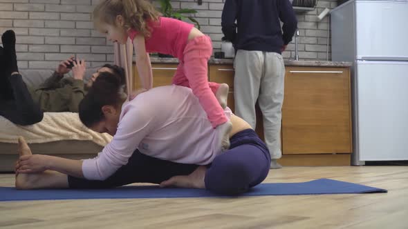 A Mother Tries to Do Yoga at Home in the Kitchen with Her Baby Daughter