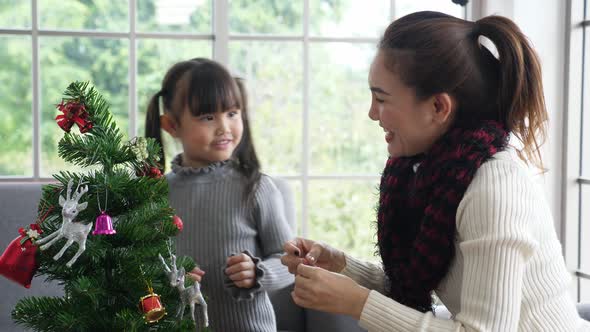 Asian mother and daughter in sweather, decorating christmas tree in living room