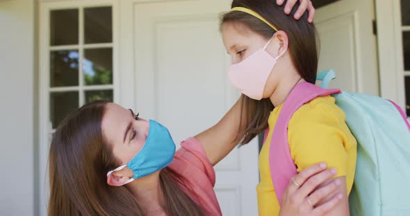 Caucasian mother wearing face mask embracing her daughter outside of the house