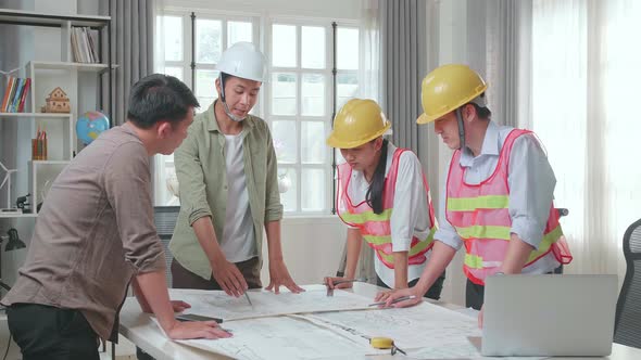 Three Asian Engineers With Helmets Presenting Work To A Man At The Office