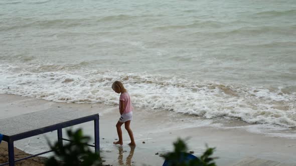 A Child Walks Along the Seashore in the Rain