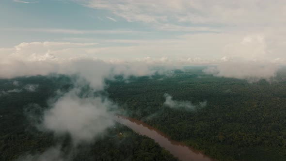 Aerial panorama view of clouds hovering over amazon rainforest and river during sunny day in Peru