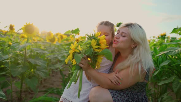 Mother and daughter sing in bouquet flowers on sunflowers field. Females girls have fun outdoors