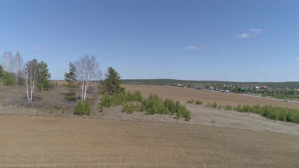 The camera flies low over a plowed field. Sunny spring day. Blue sky. The camera flies back