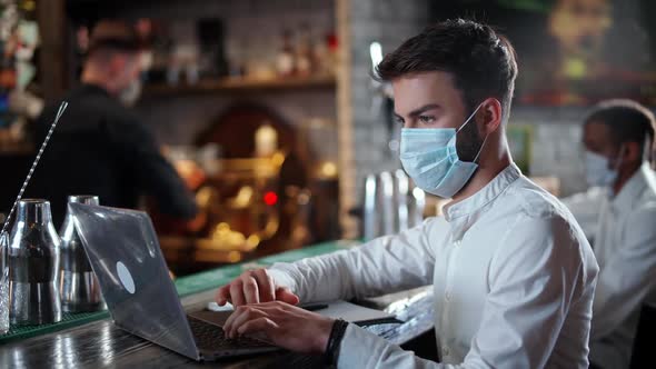 Freelancer Works Outside the Home a Young Man Developer in a Medical Mask Sits at the Bar and Works