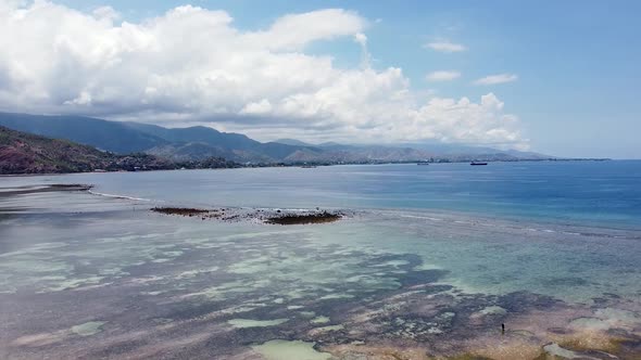 Aerial drone rising over solo fishermen at low tide in crystal clear water with stunning sand bars a