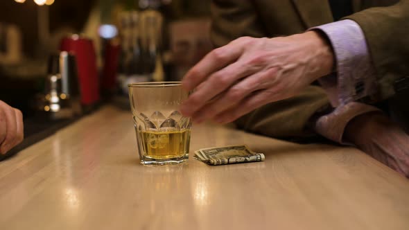 A bar visitor pays for the drink in cash. Close-up of exchanging whiskey for dollars