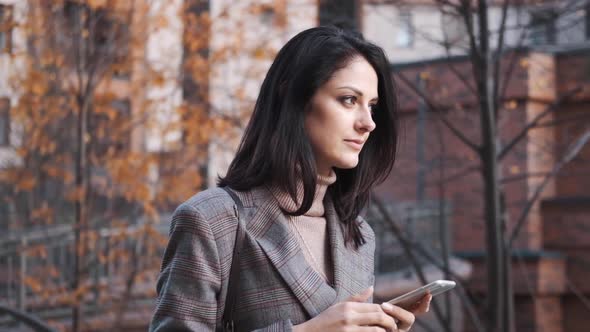 Portrait of a Confident Business Woman in a Suit Uses a Smartphone Outdoors