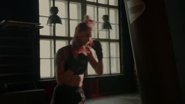 Athletic Fit Female Boxer Exercising Punches with Boxing Bag in Gym During Kickboxing