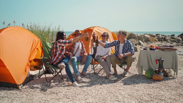 Four Friends on Picnic Drinking Cold Beer and Clinking Bottles at Hot Sunny Day on Beach